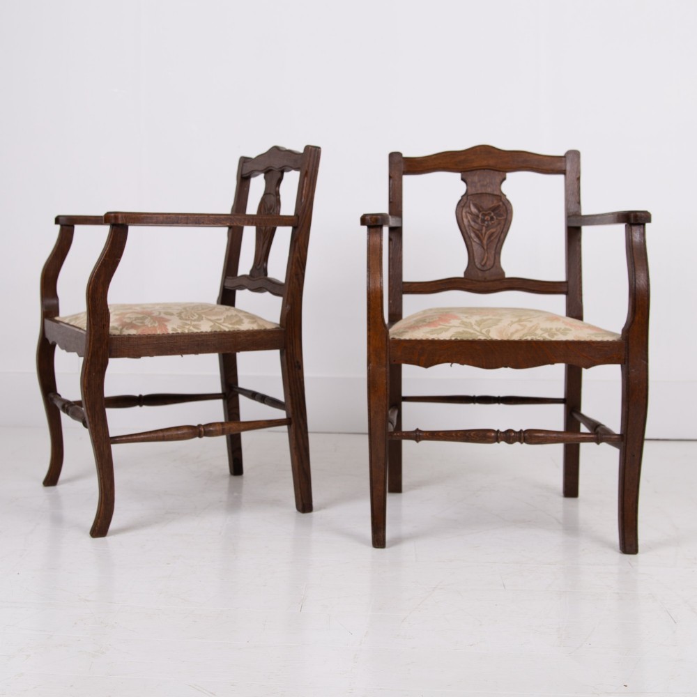 A pair of dark oak open armchairs featuring carved floral back splats, curved arms, turned stretchers, and light floral upholstered seats. View XII