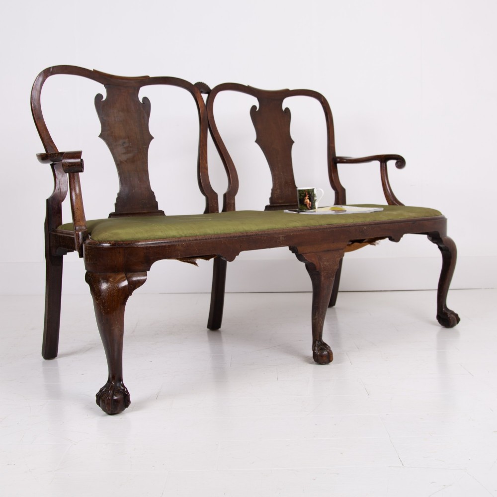 A George II revival double chair-back mahogany settee featuring carved vase splats, cabriole legs with claw and ball feet, and a green upholstered seat.