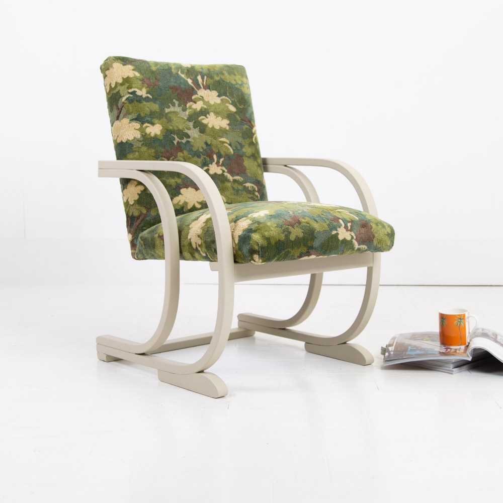 An Art Deco armchair featuring curved off-white painted bentwood arms and frame with green foliage pattern fabric upholstery on the seat and back.