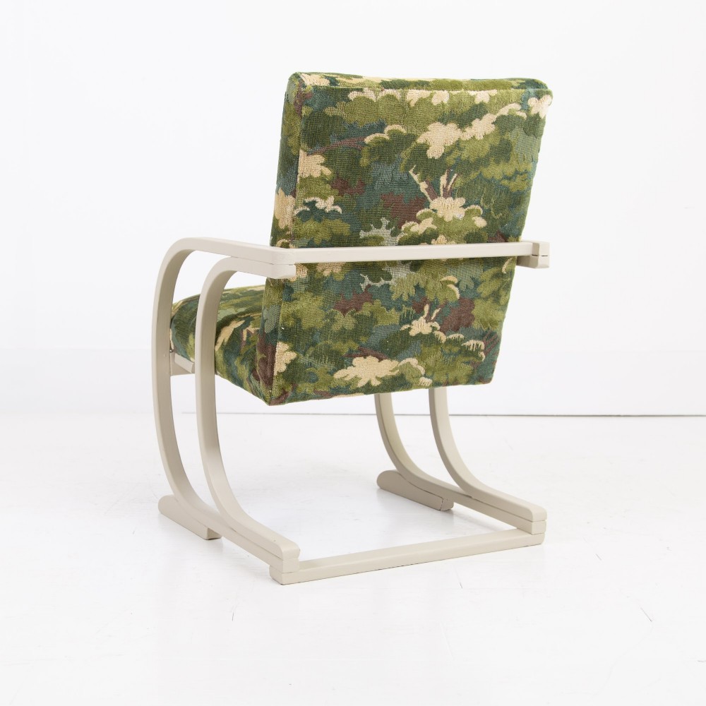 An Art Deco armchair featuring curved off-white painted bentwood arms and frame with green foliage pattern fabric upholstery on the seat and back. View III