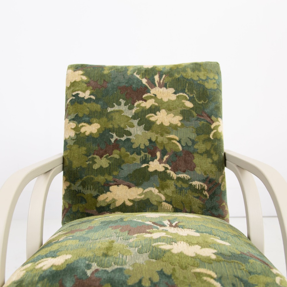 An Art Deco armchair featuring curved off-white painted bentwood arms and frame with green foliage pattern fabric upholstery on the seat and back. View VI