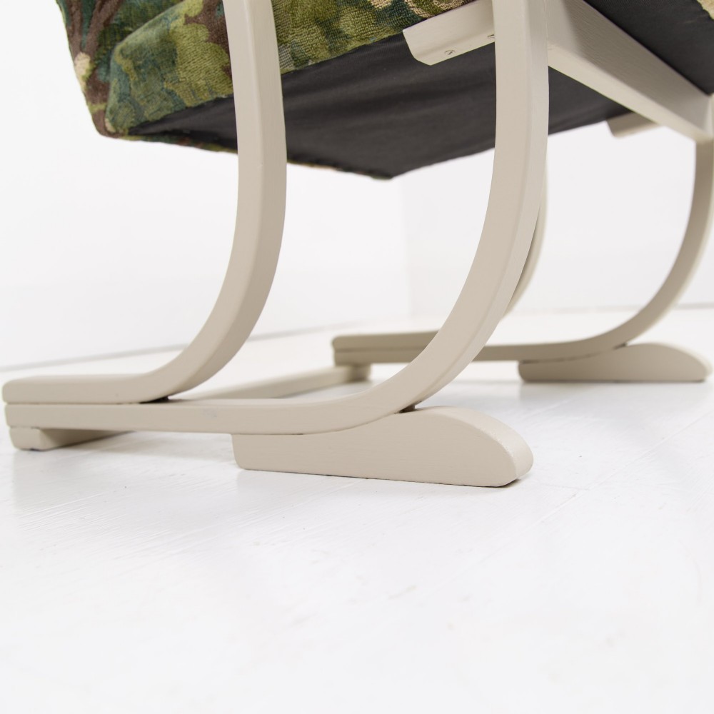 An Art Deco armchair featuring curved off-white painted bentwood arms and frame with green foliage pattern fabric upholstery on the seat and back. View IX