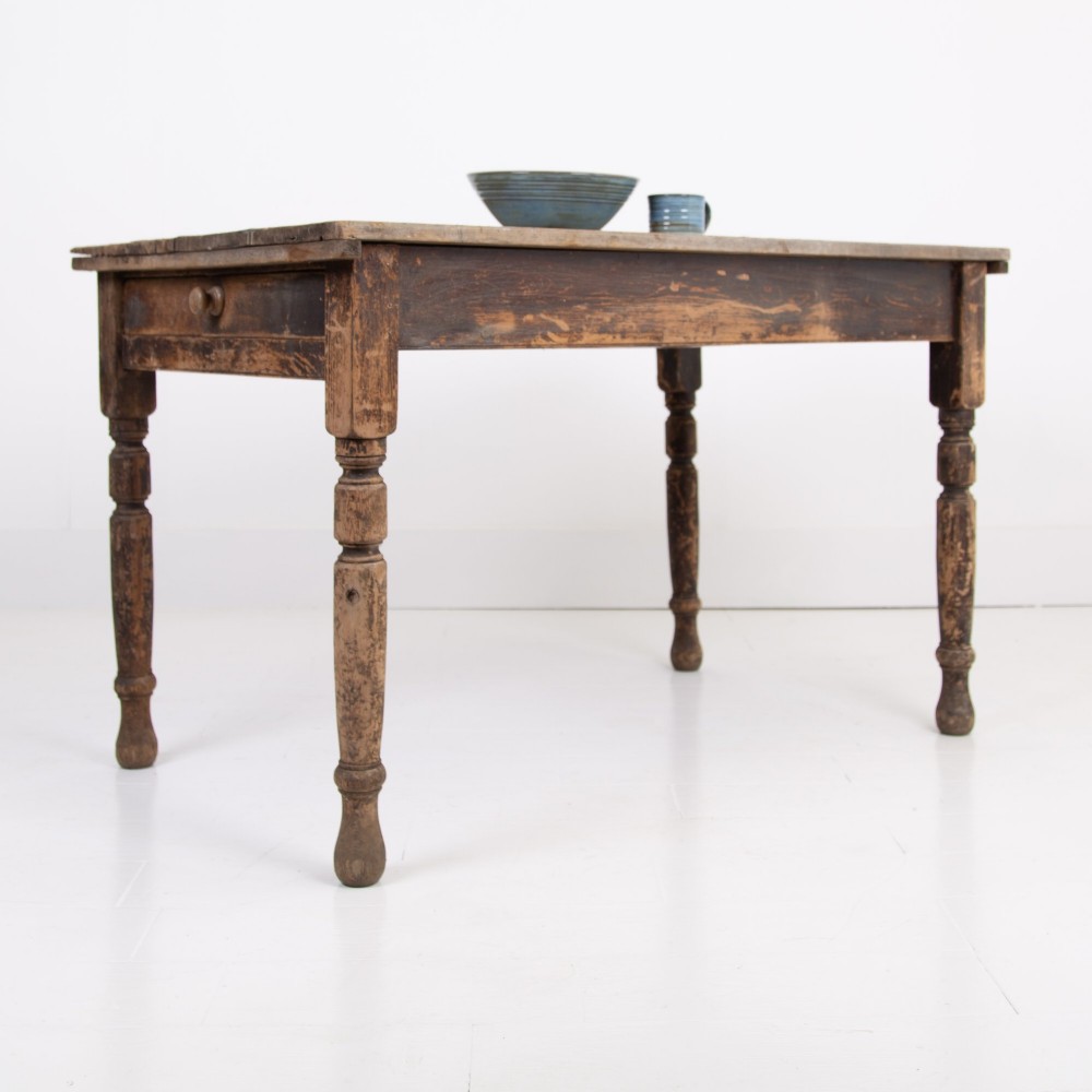 A late Victorian rustic wooden kitchen table featuring turned legs, a single drawer, and a distressed dark finish.