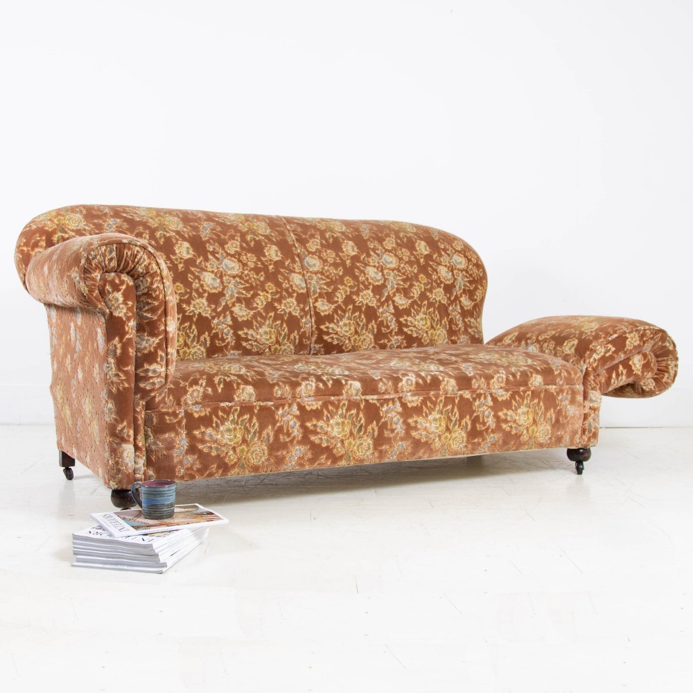 A late 1920s three-seater sofa upholstered in brown floral velvet, featuring a drop-arm end on turned wooden legs with castors. View III