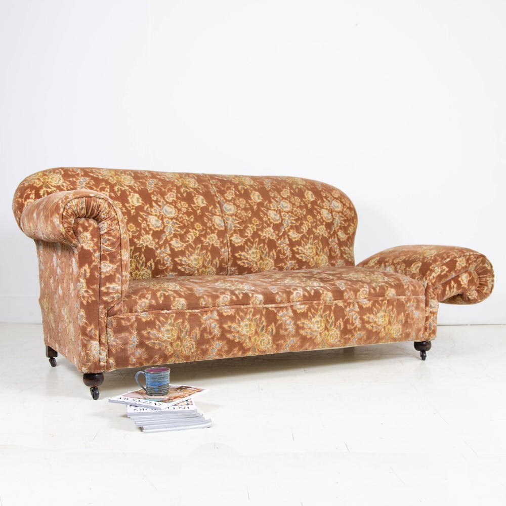 A late 1920s three-seater sofa upholstered in brown floral velvet, featuring a drop-arm end on turned wooden legs with castors. View IV