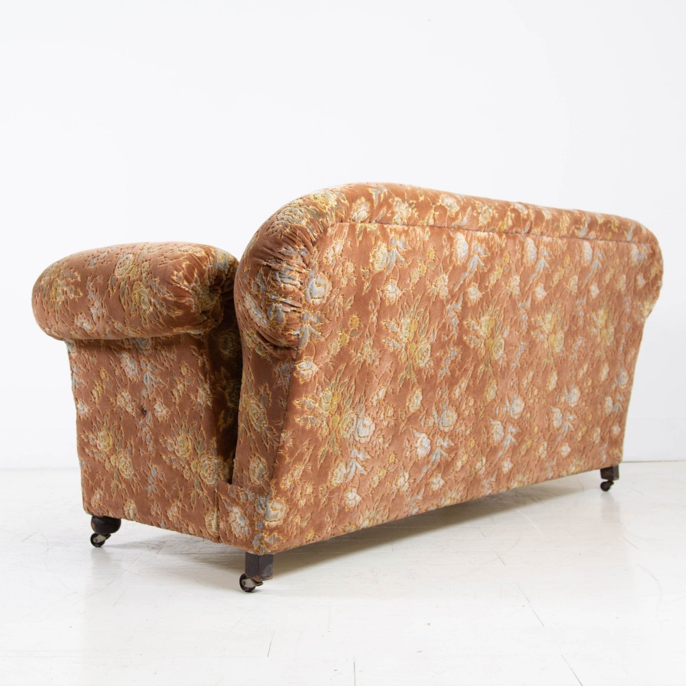 A late 1920s three-seater sofa upholstered in brown floral velvet, featuring a drop-arm end on turned wooden legs with castors. View VIII