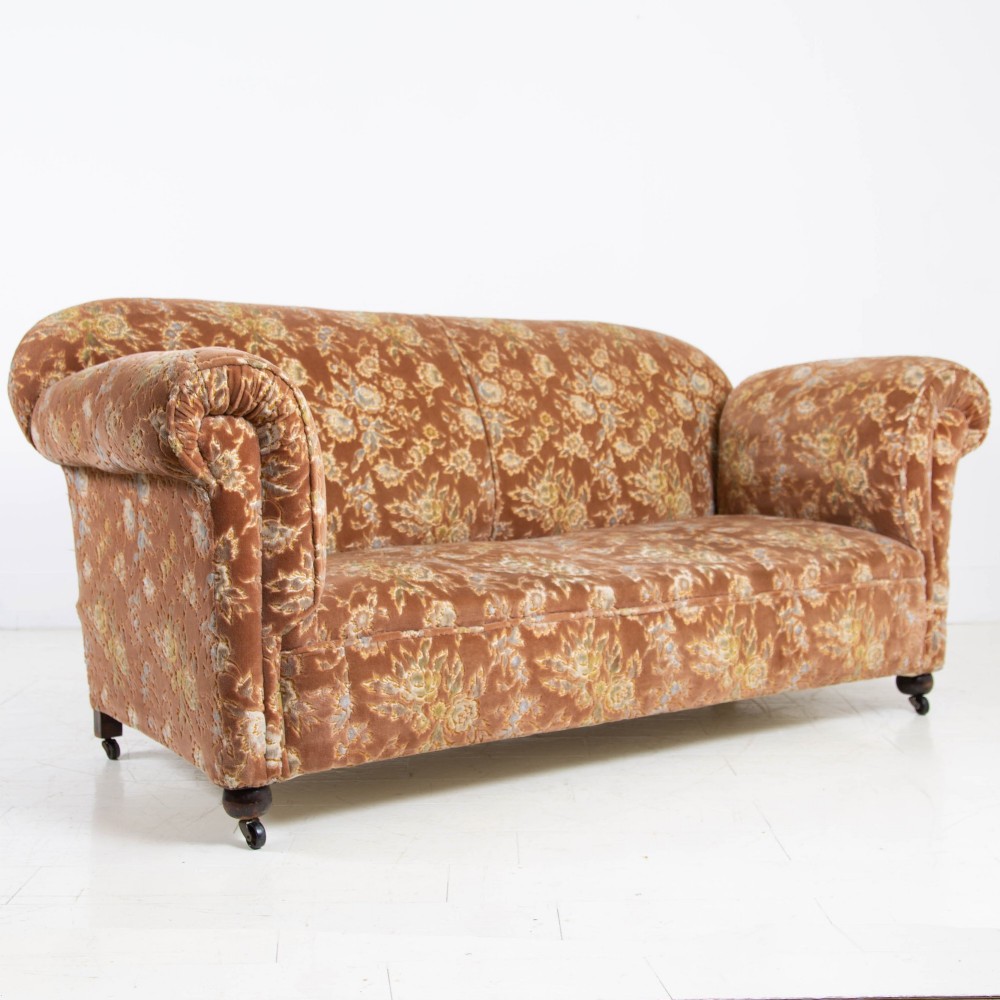 A late 1920s three-seater sofa upholstered in brown floral velvet, featuring a drop-arm end on turned wooden legs with castors. View IX