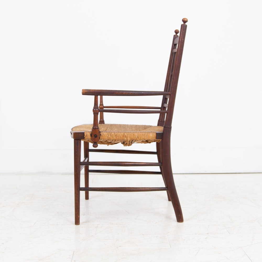An antique Arts and Crafts wooden armchair featuring turned spindle backrest slats, sloped armrests, turned finials, and a hand-woven natural rush seat. View II