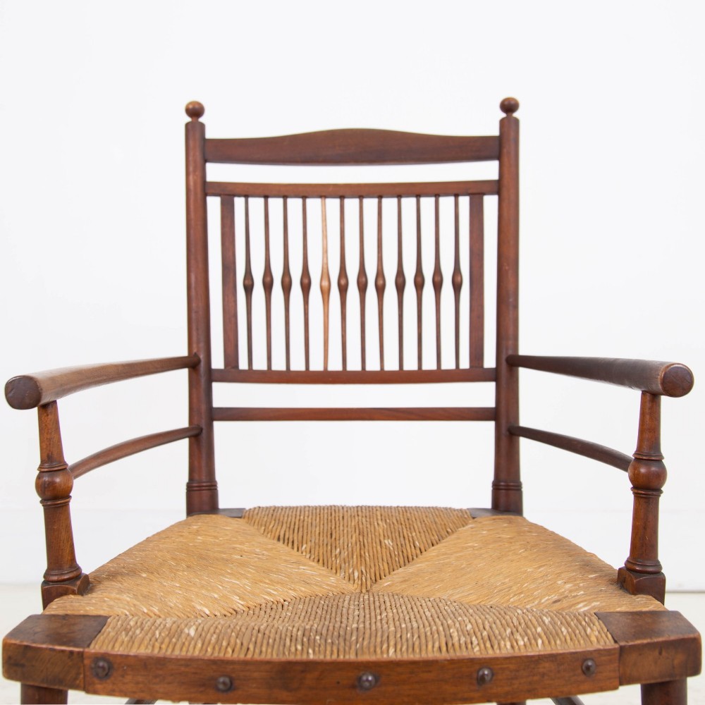 An antique Arts and Crafts wooden armchair featuring turned spindle backrest slats, sloped armrests, turned finials, and a hand-woven natural rush seat. View IV