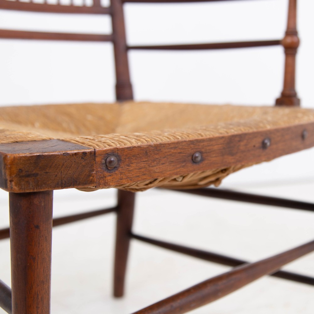 An antique Arts and Crafts wooden armchair featuring turned spindle backrest slats, sloped armrests, turned finials, and a hand-woven natural rush seat. View V