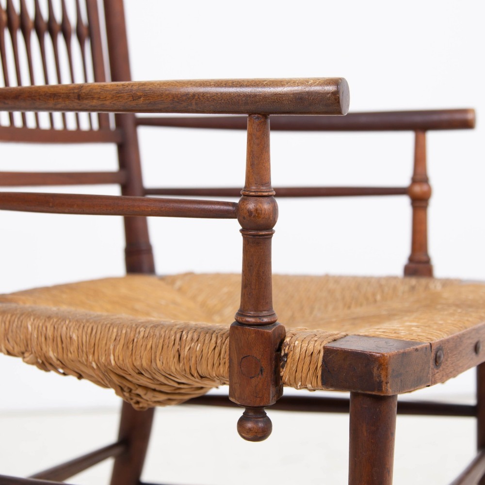 An antique Arts and Crafts wooden armchair featuring turned spindle backrest slats, sloped armrests, turned finials, and a hand-woven natural rush seat. View IX