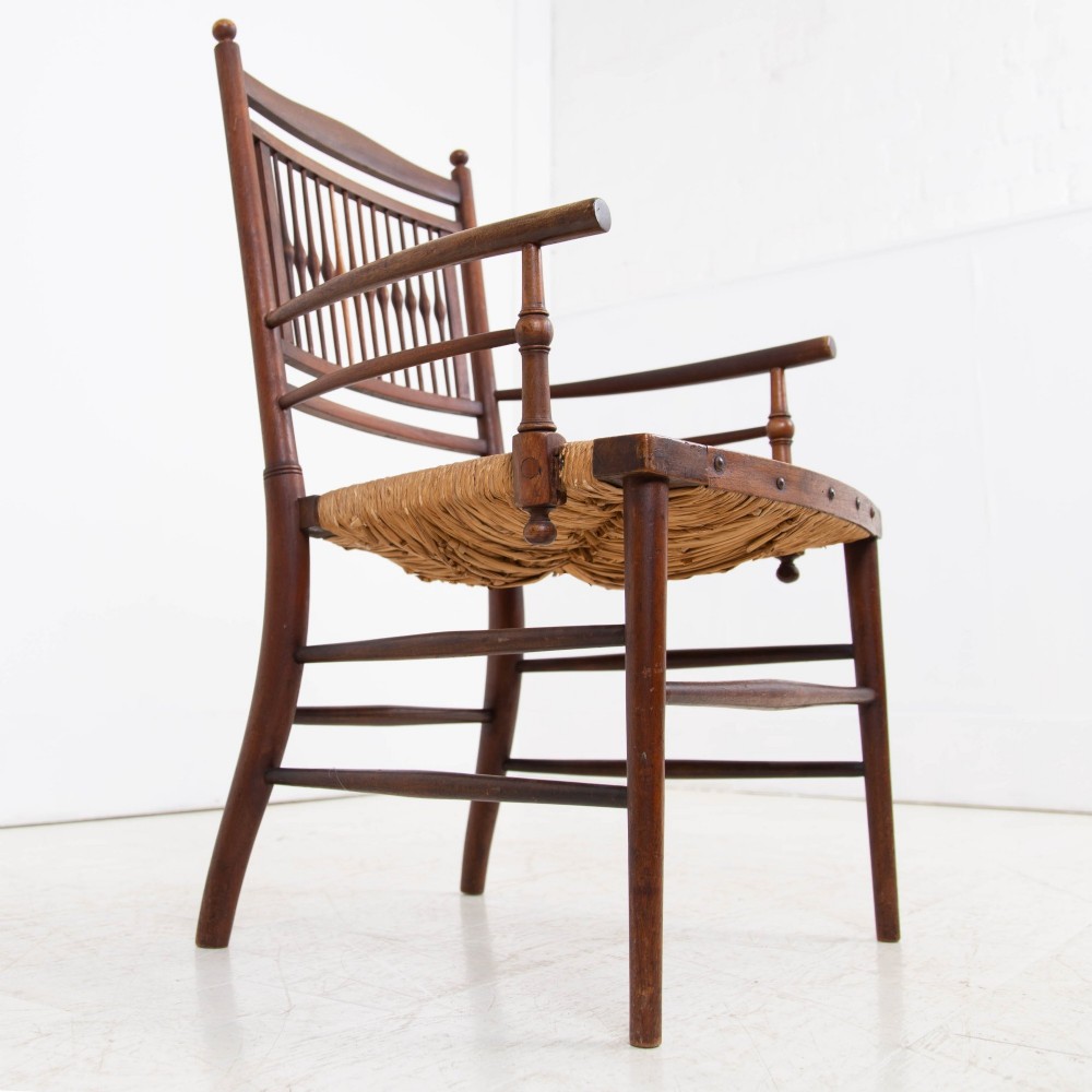 An antique Arts and Crafts wooden armchair featuring turned spindle backrest slats, sloped armrests, turned finials, and a hand-woven natural rush seat. View XI