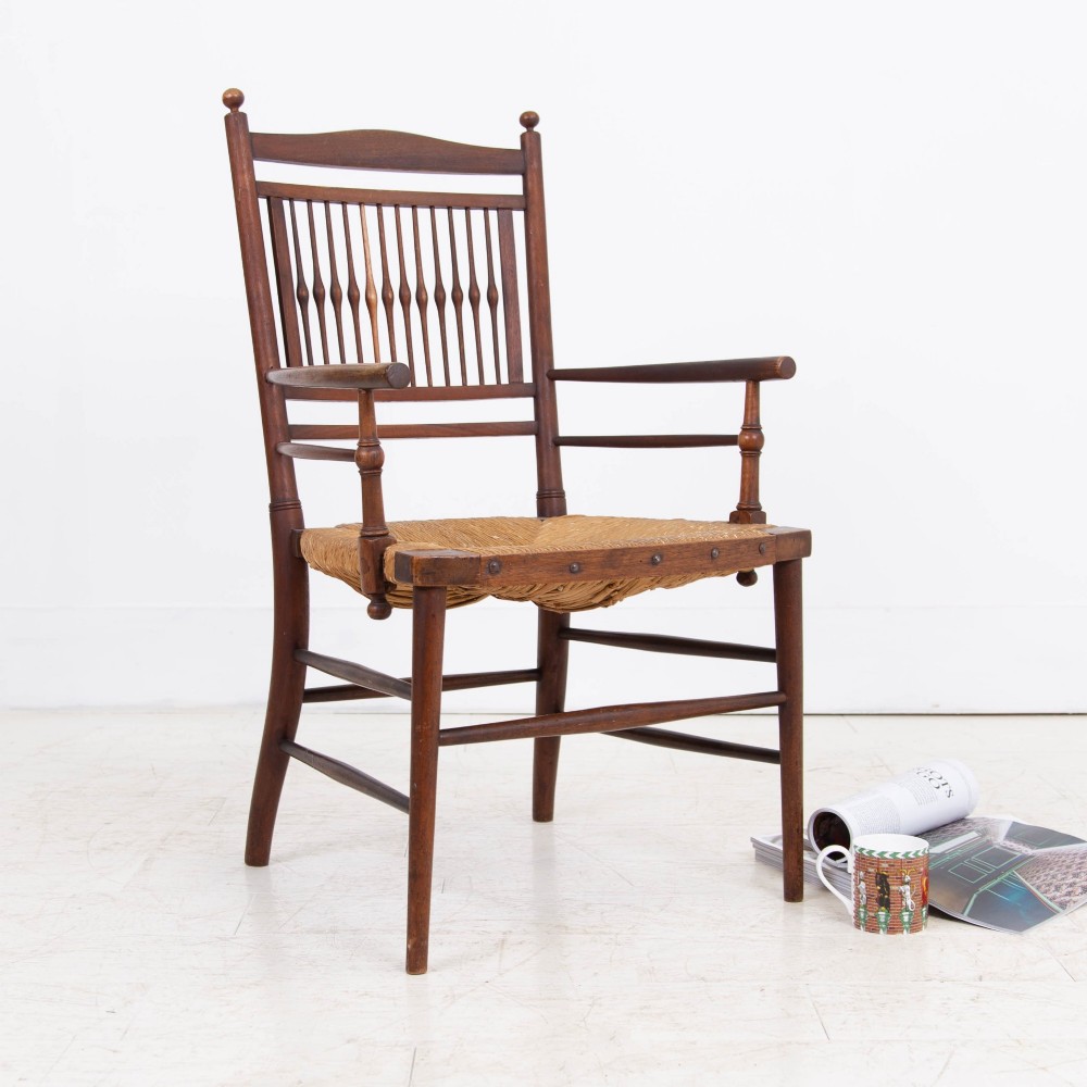 An antique Arts and Crafts wooden armchair featuring turned spindle backrest slats, sloped armrests, turned finials, and a hand-woven natural rush seat. View XII