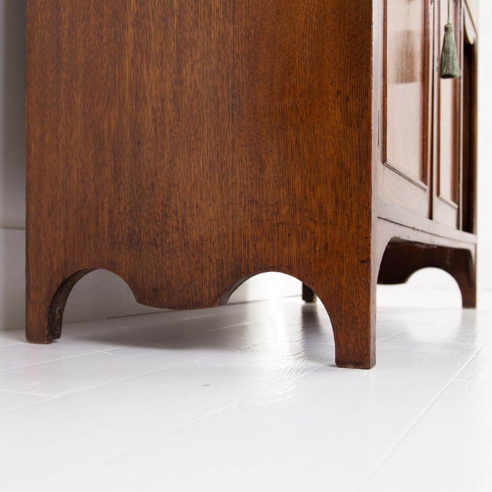 An Arts and Crafts oak cabinet dresser featuring an upper shelf unit with a central leaded glass door above a base section with a single drawer, cupboard doors, and an open side alcove. View XI