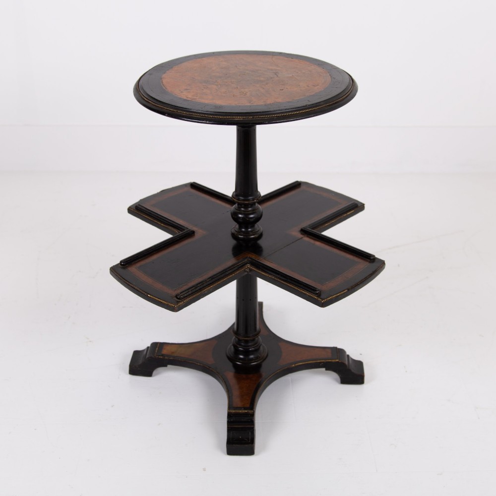 A Victorian ebonised side table featuring a circular top inlaid with amboyna wood, a central turned column, a lower cruciform tier, and a four-point flared base.
