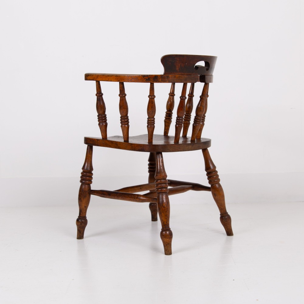 An antique 19th-century wooden smokers bow armchair with turned spindles, a curved horseshoe armrest, and a shaped seat. View V