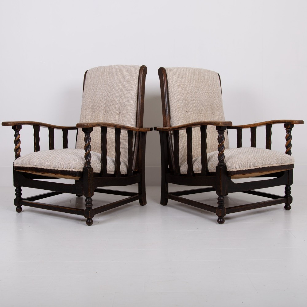 A pair of dark oak reclining armchairs with barley twist front supports, slatted sides, and beige textured upholstery.