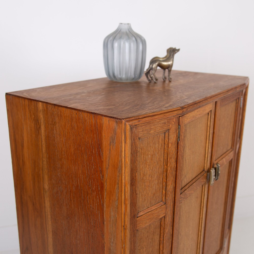 A 1930s Art Deco oak tallboy cabinet featuring a two-door upper cupboard with geometric paneling above two wide drawers, resting on stylized stepped feet. View III