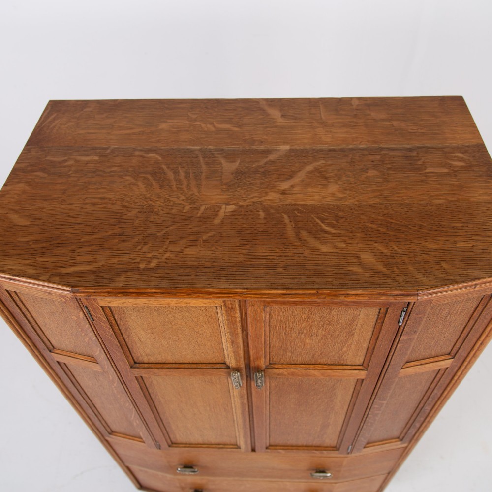 A 1930s Art Deco oak tallboy cabinet featuring a two-door upper cupboard with geometric paneling above two wide drawers, resting on stylized stepped feet. View IX