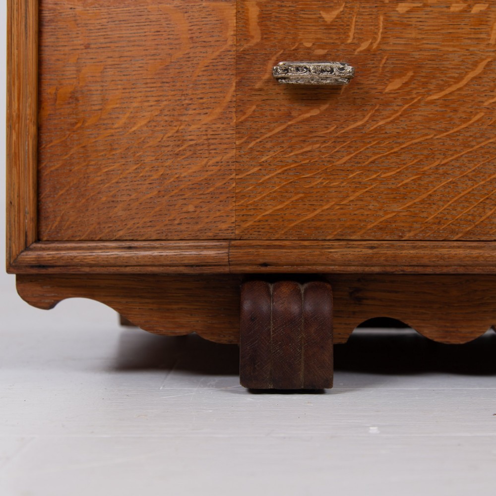 A 1930s Art Deco oak tallboy cabinet featuring a two-door upper cupboard with geometric paneling above two wide drawers, resting on stylized stepped feet. View XI