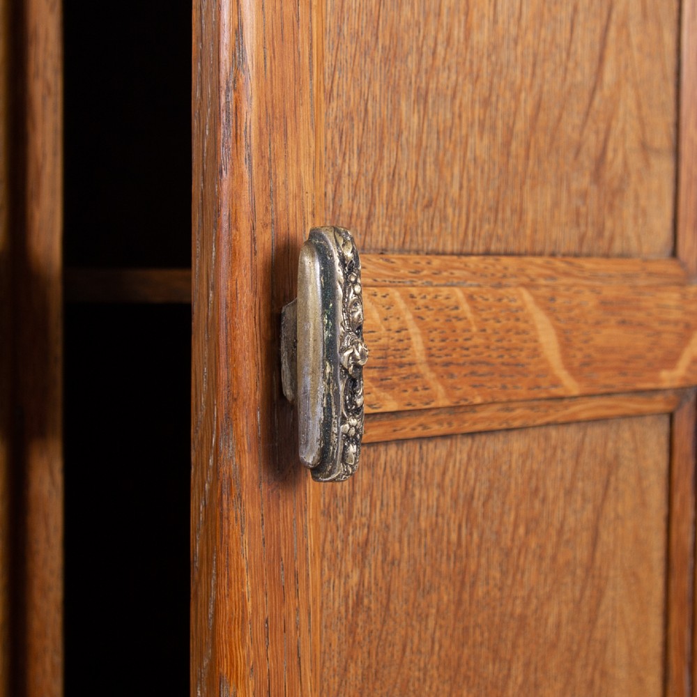 A 1930s Art Deco oak tallboy cabinet featuring a two-door upper cupboard with geometric paneling above two wide drawers, resting on stylized stepped feet. View XII