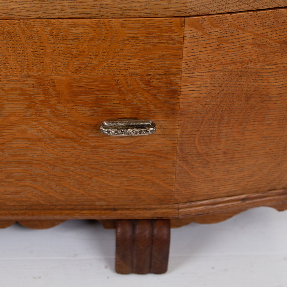 A 1930s Art Deco oak tallboy cabinet featuring a two-door upper cupboard with geometric paneling above two wide drawers, resting on stylized stepped feet. View XIII