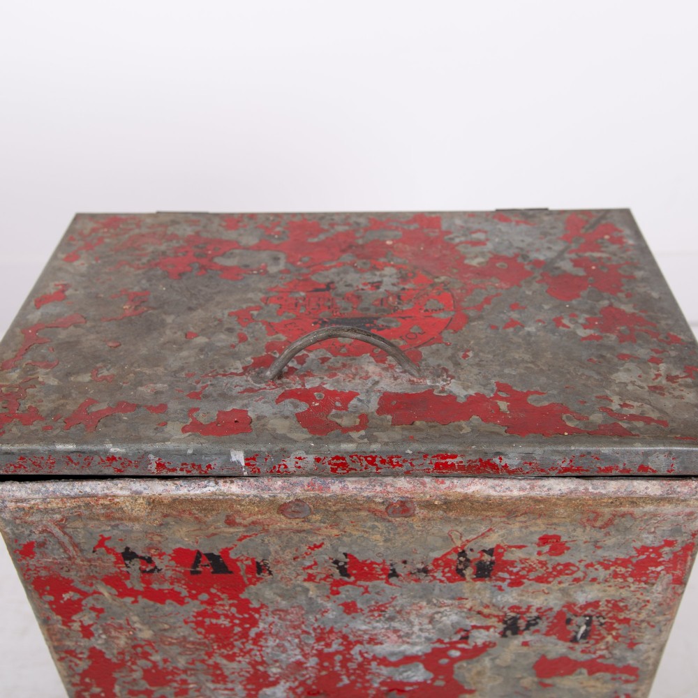 A tall rectangular industrial metal fire bin with distressed red paint, stencilled black text, a top lid, and four small cast iron swivel castors. View III