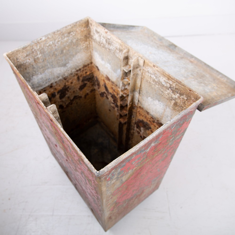 A tall rectangular industrial metal fire bin with distressed red paint, stencilled black text, a top lid, and four small cast iron swivel castors. View X