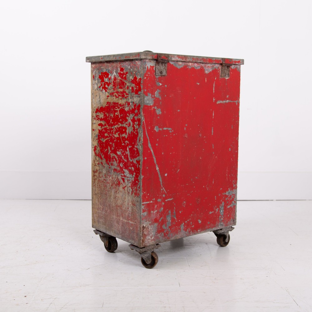 A tall rectangular industrial metal fire bin with distressed red paint, stencilled black text, a top lid, and four small cast iron swivel castors. View XI