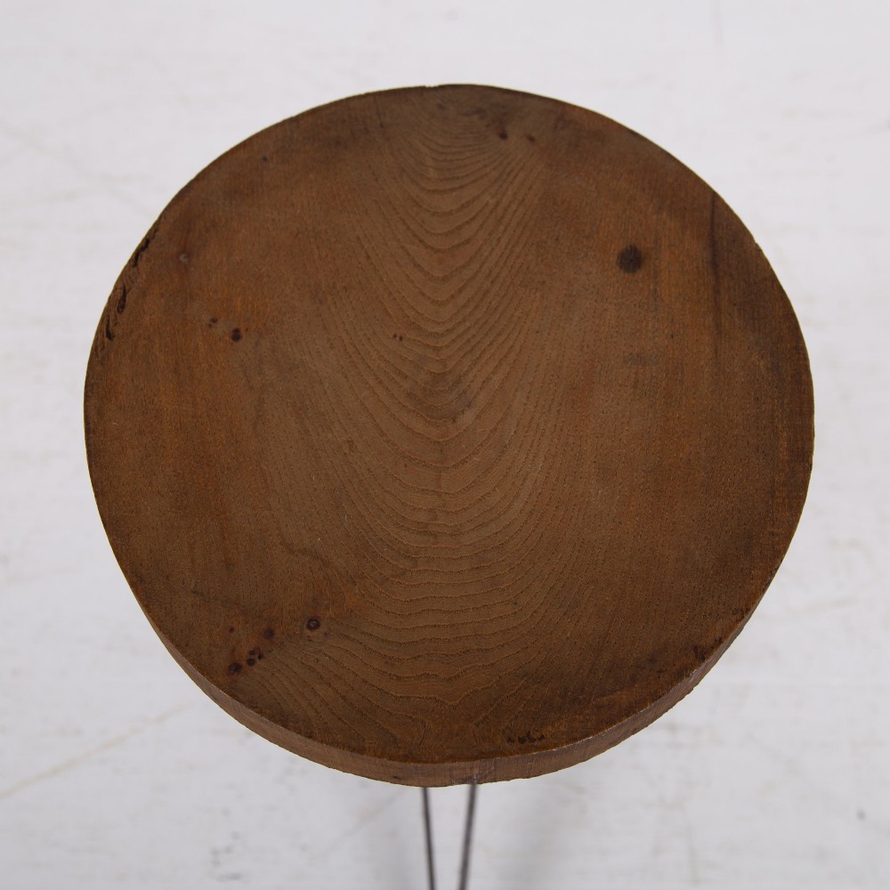 An industrial 1930s workshop stool featuring a circular wooden seat mounted on a dark brown metal tripod base with a threaded height adjustment mechanism. View VI