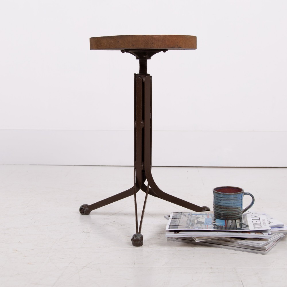 An industrial 1930s workshop stool featuring a circular wooden seat mounted on a dark brown metal tripod base with a threaded height adjustment mechanism. View VIII