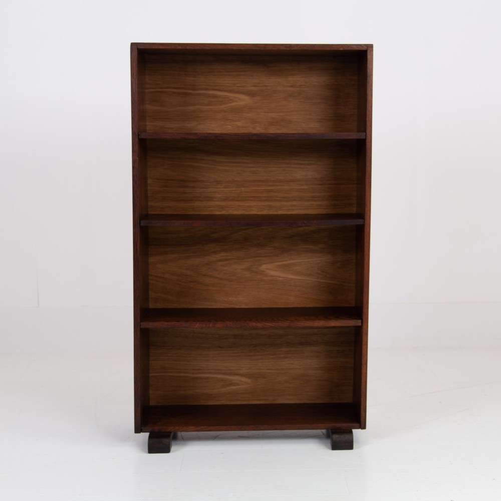 A 1930s open oak bookcase featuring four tier shelf sections and dark block feet against a plain background.