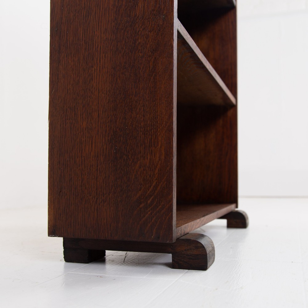 A 1930s open oak bookcase featuring four tier shelf sections and dark block feet against a plain background. View IV