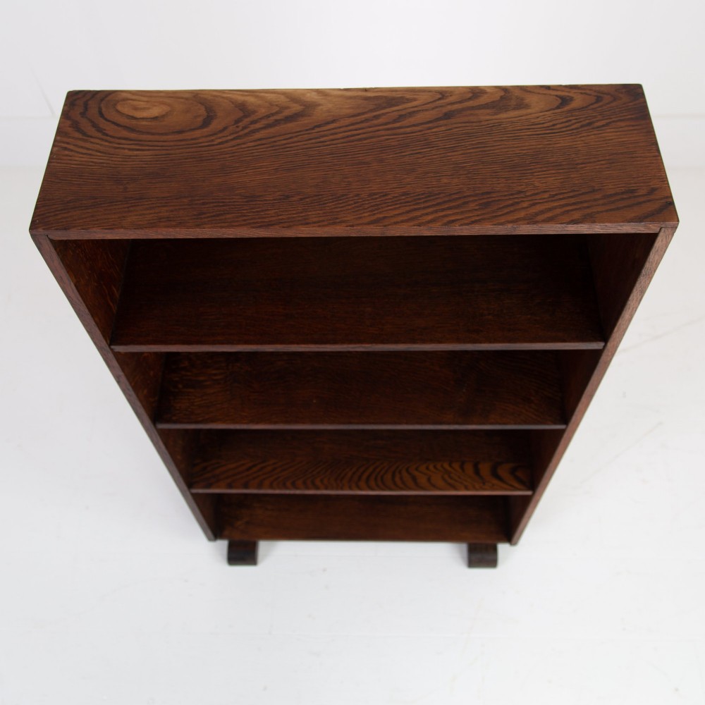 A 1930s open oak bookcase featuring four tier shelf sections and dark block feet against a plain background. View V