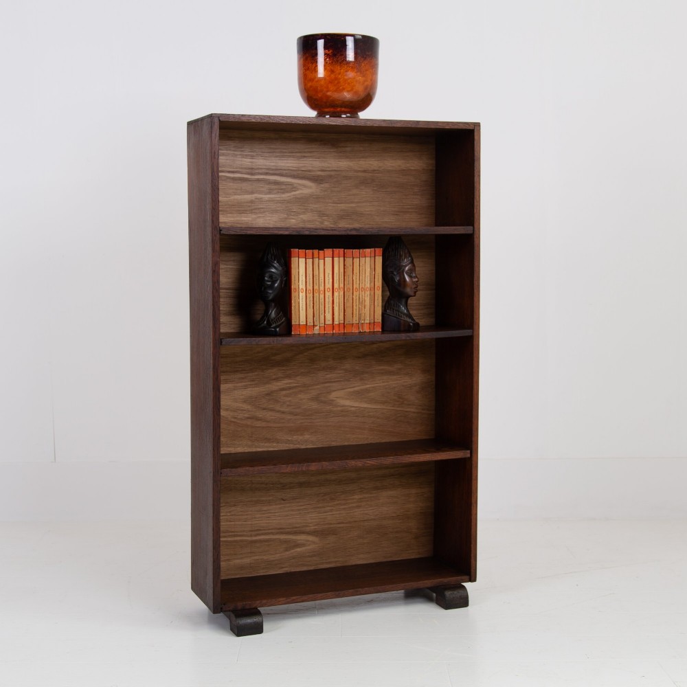 A 1930s open oak bookcase featuring four tier shelf sections and dark block feet against a plain background. View X