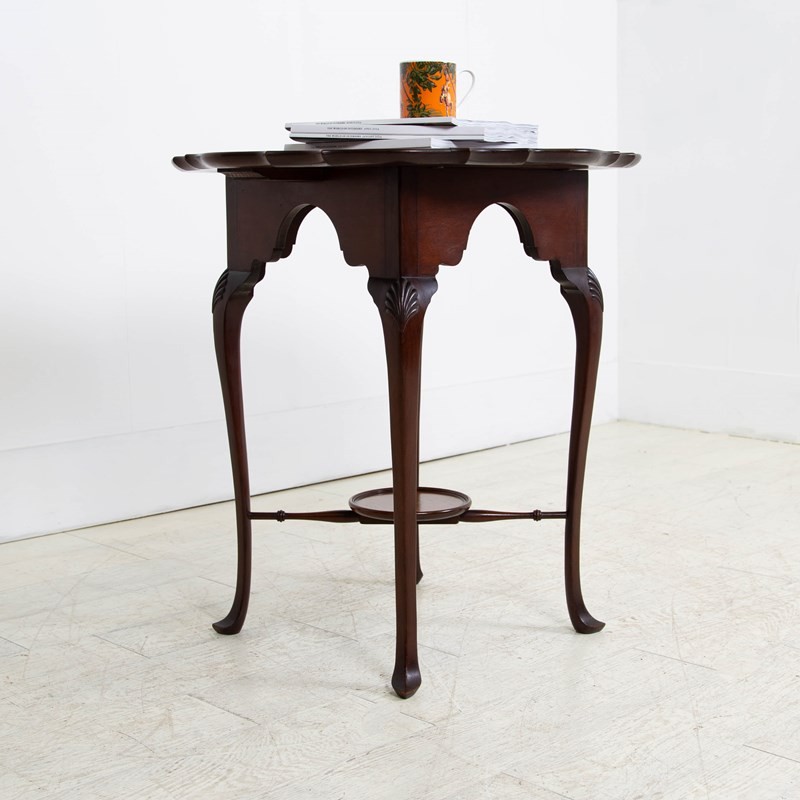 An antique dark mahogany side table featuring a scalloped piecrust top, arched aprons, slender cabriole legs with shell-carved knees, and a central circular lower tier.