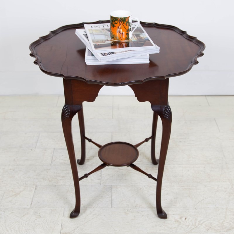 An antique dark mahogany side table featuring a scalloped piecrust top, arched aprons, slender cabriole legs with shell-carved knees, and a central circular lower tier. View II
