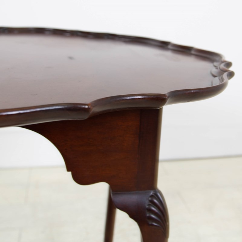 An antique dark mahogany side table featuring a scalloped piecrust top, arched aprons, slender cabriole legs with shell-carved knees, and a central circular lower tier. View III