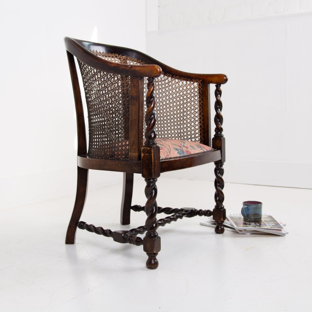 A dark wood Jacobean Revival tub armchair featuring woven cane panelling, carved barley twist legs, and a floral upholstered seat.