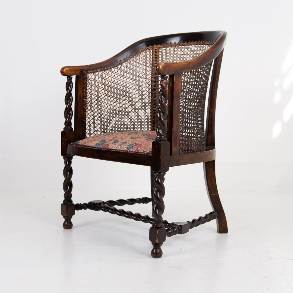 A dark wood Jacobean Revival tub armchair featuring woven cane panelling, carved barley twist legs, and a floral upholstered seat. View II