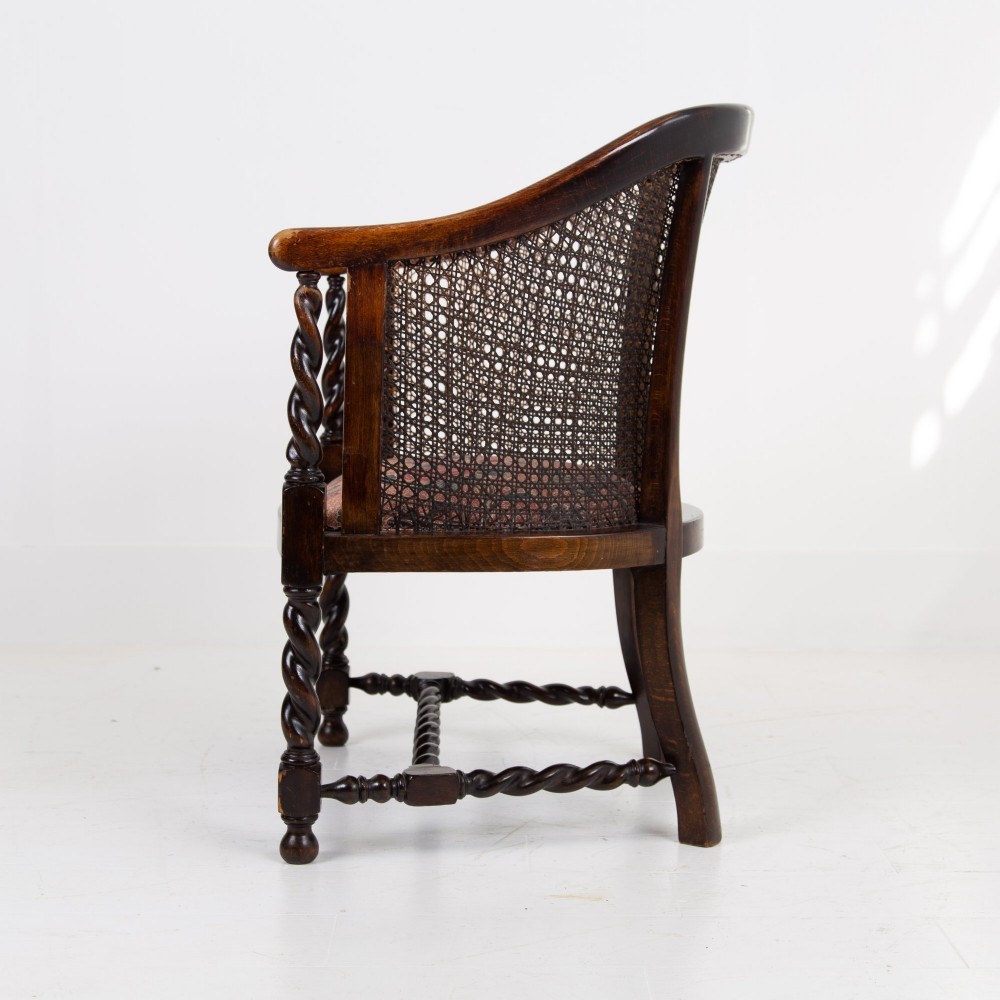 A dark wood Jacobean Revival tub armchair featuring woven cane panelling, carved barley twist legs, and a floral upholstered seat. View III