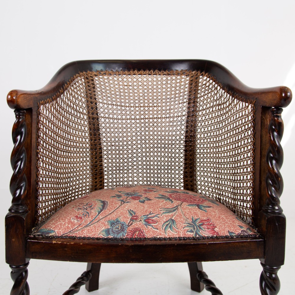 A dark wood Jacobean Revival tub armchair featuring woven cane panelling, carved barley twist legs, and a floral upholstered seat. View IV