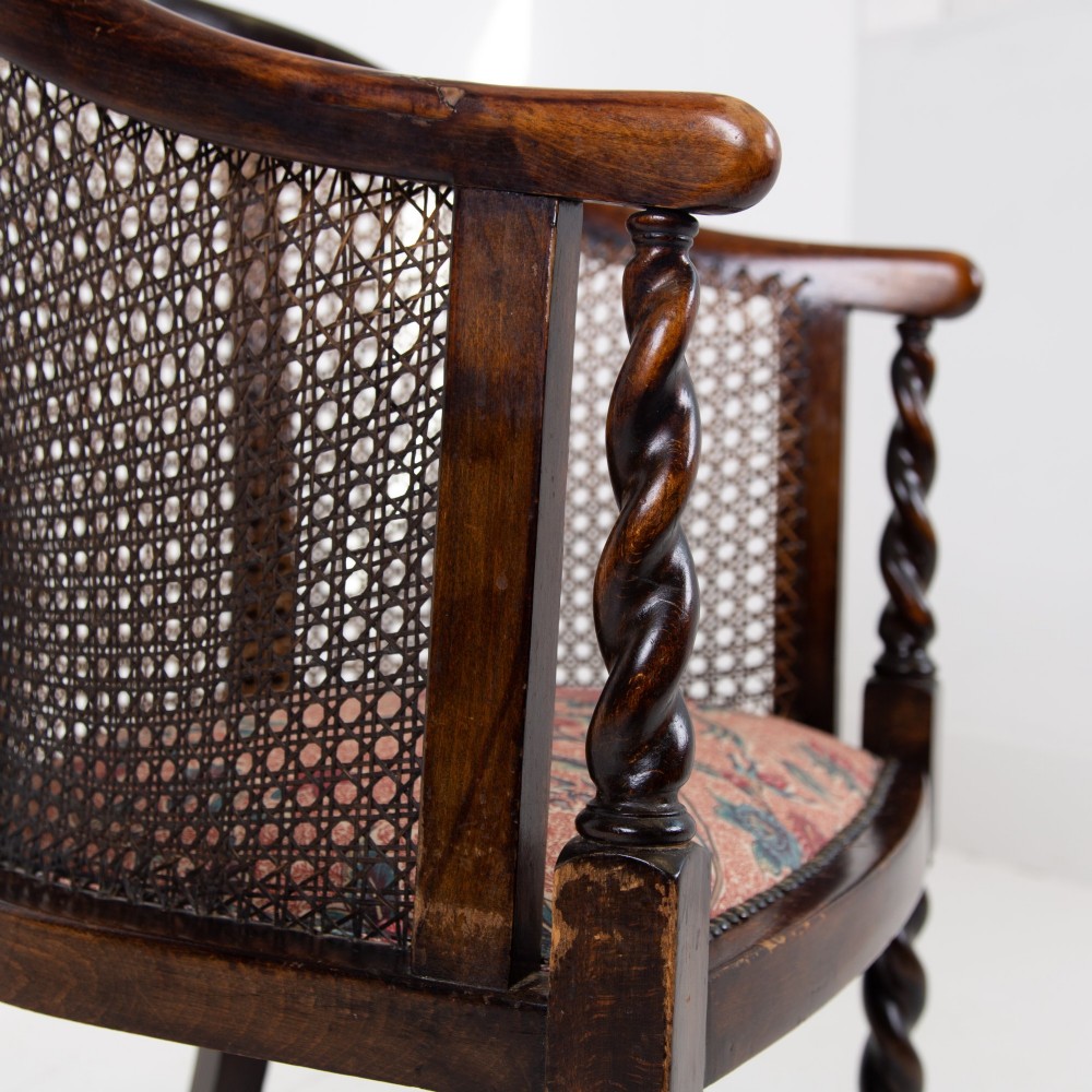 A dark wood Jacobean Revival tub armchair featuring woven cane panelling, carved barley twist legs, and a floral upholstered seat. View V