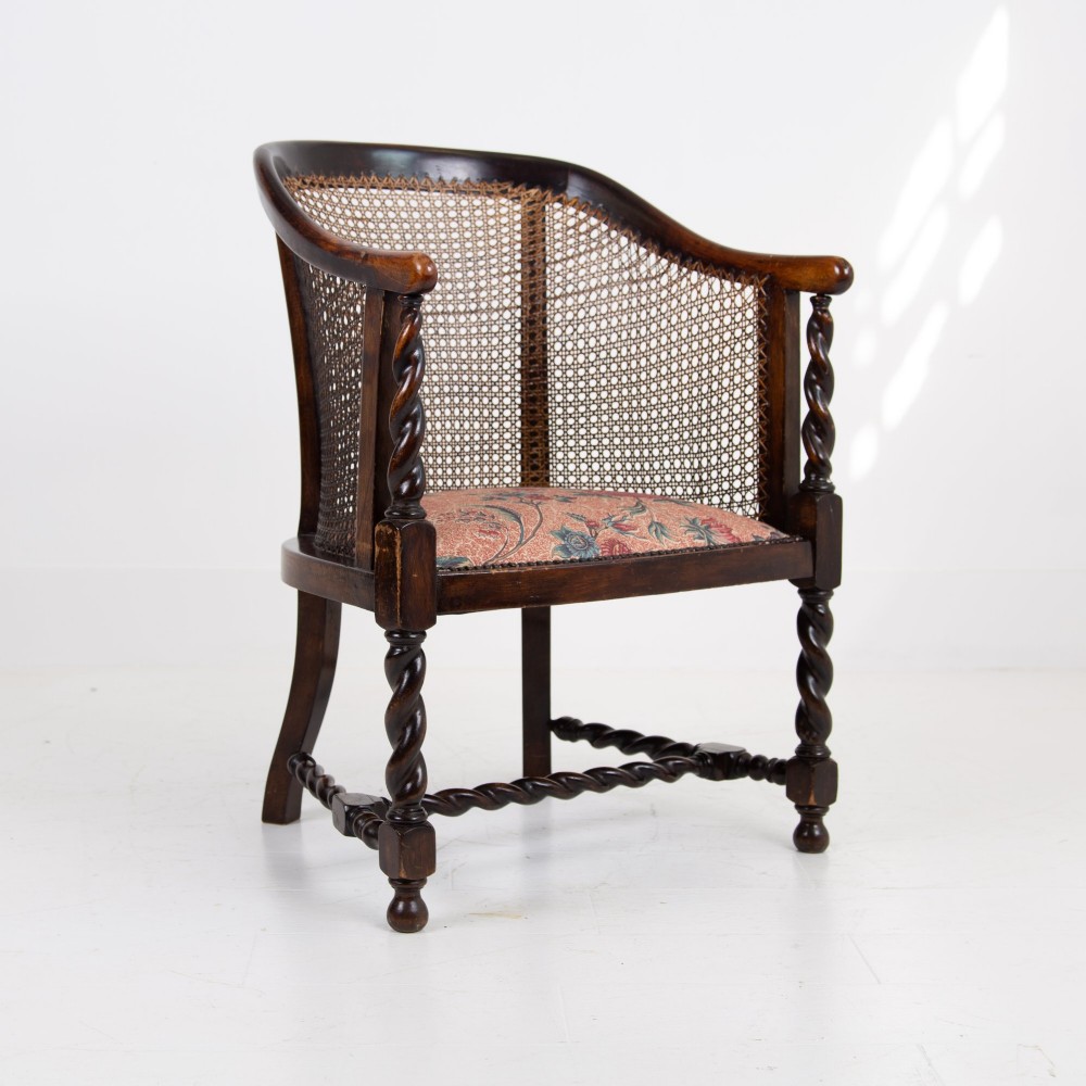 A dark wood Jacobean Revival tub armchair featuring woven cane panelling, carved barley twist legs, and a floral upholstered seat. View VI