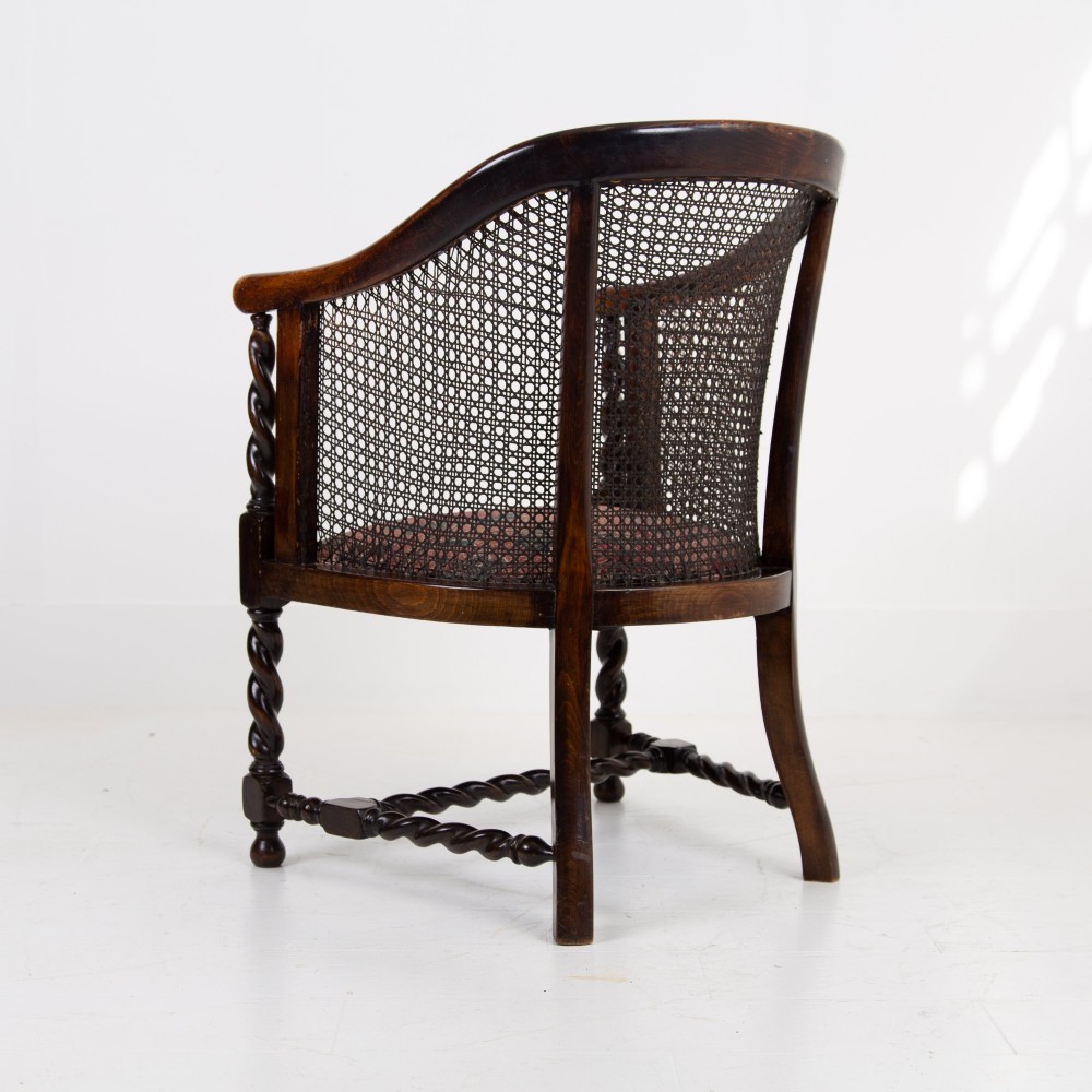 A dark wood Jacobean Revival tub armchair featuring woven cane panelling, carved barley twist legs, and a floral upholstered seat. View IX