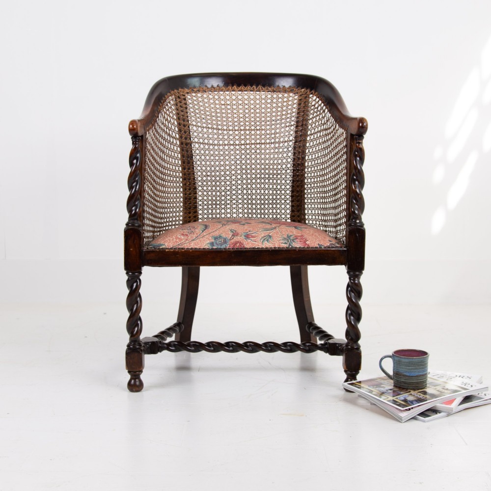 A dark wood Jacobean Revival tub armchair featuring woven cane panelling, carved barley twist legs, and a floral upholstered seat. View X
