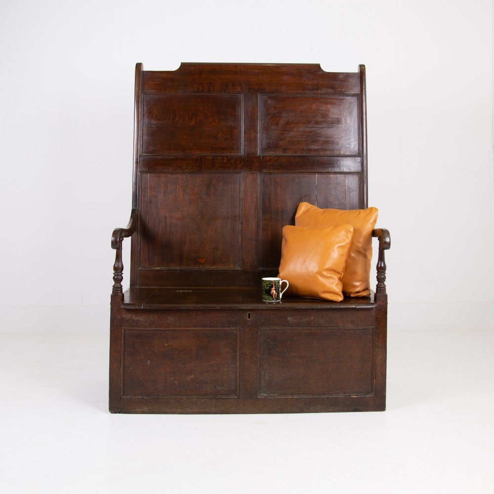 A 19th-century dark oak high-back box settle with panelled detailing, scrolled armrests, turned supports, and a hinged seat opening to a box storage base. View II