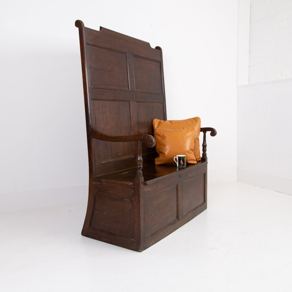 A 19th-century dark oak high-back box settle with panelled detailing, scrolled armrests, turned supports, and a hinged seat opening to a box storage base. View III