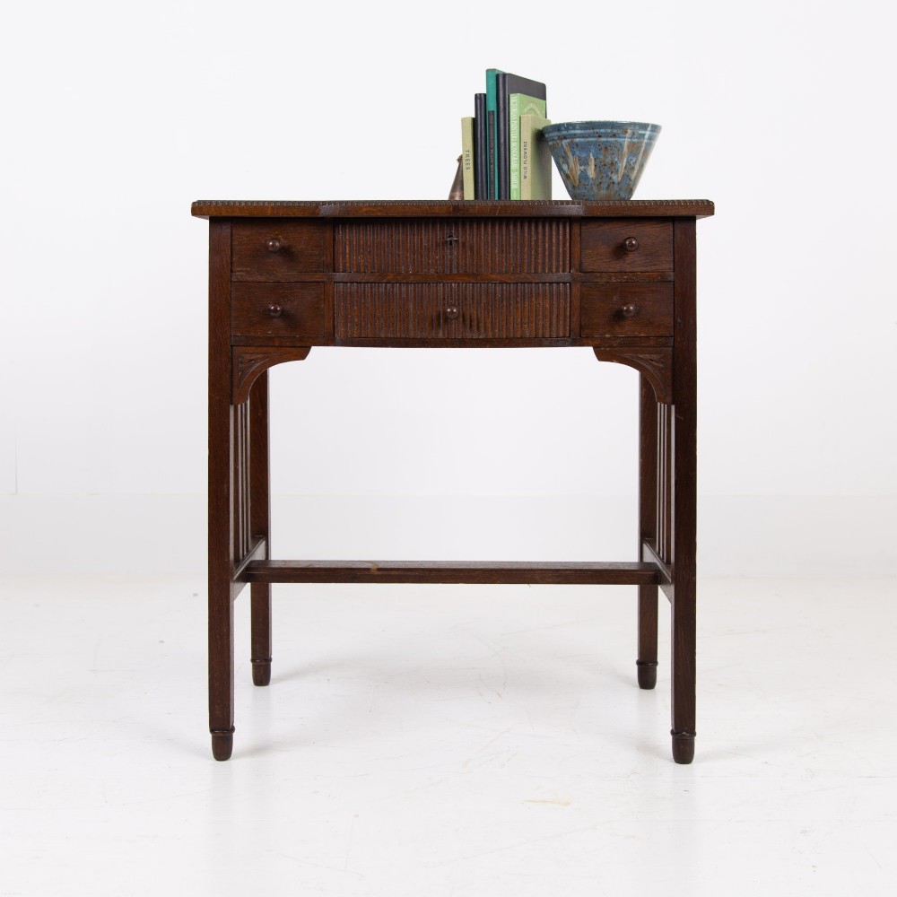 A 1930s Art Deco dark oak side table featuring six small drawers with fluted fronts and turned wooden handles, supported by tall legs and an H-stretcher.