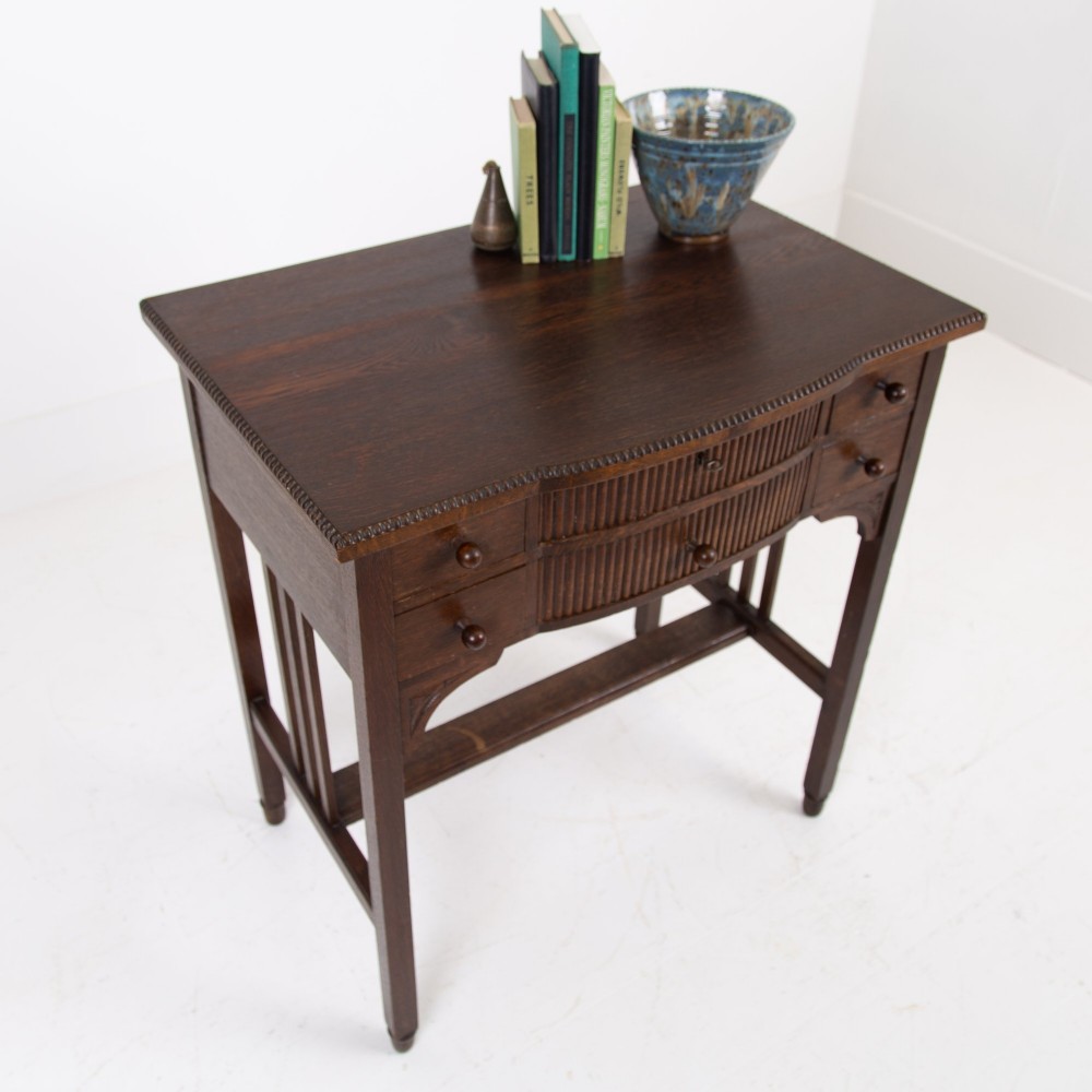 A 1930s Art Deco dark oak side table featuring six small drawers with fluted fronts and turned wooden handles, supported by tall legs and an H-stretcher. View III